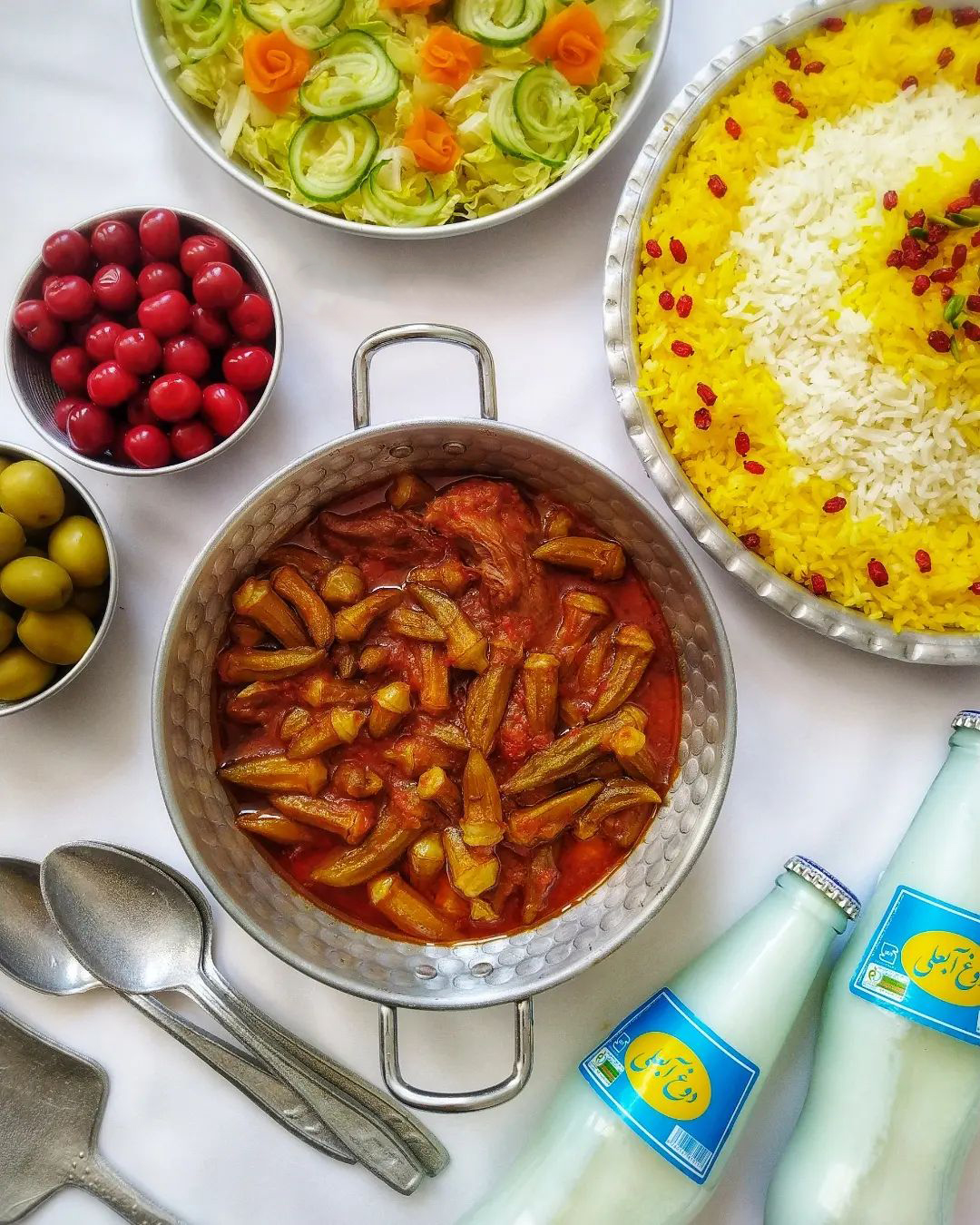 خورش بامیه که به همراه برنج و مخلفاتی همچون دوغ، سالاد، زیتون و ترشی سرو شده است.