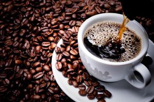 یک فنجان قهوه به همراه دانه‌های قهوه در اطراف آن .jpg